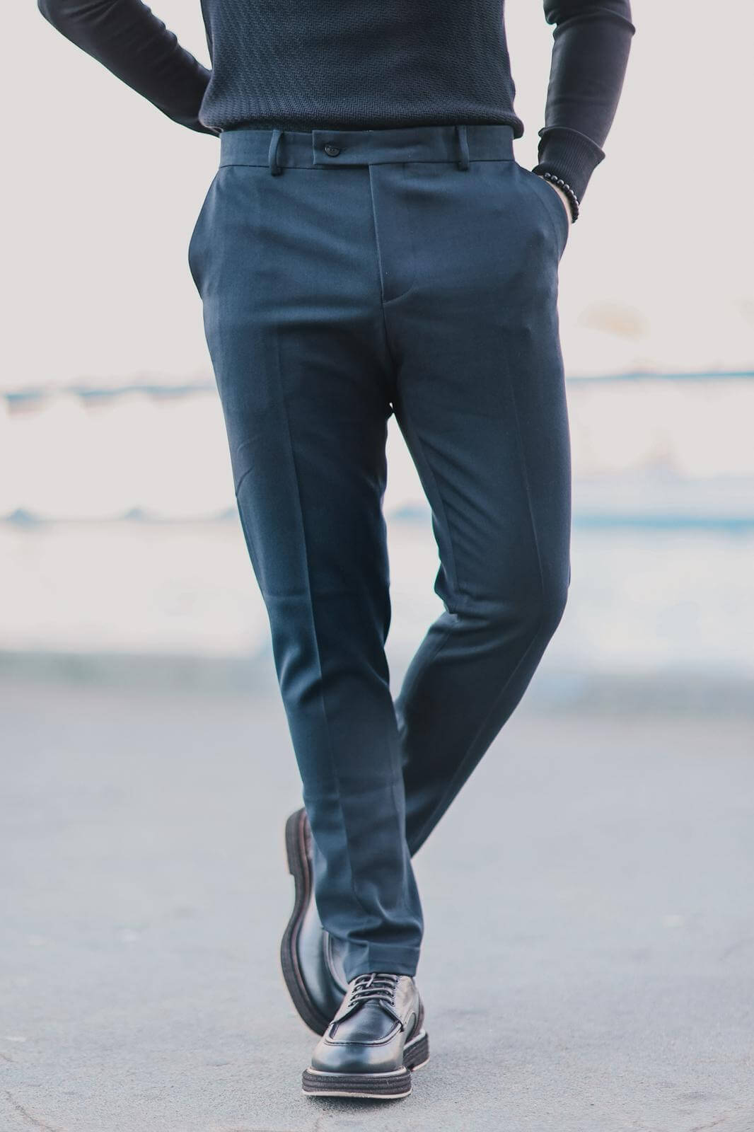 Men wearing navy blue slim-fit trousers paired with black derby shoes, standing outdoors in a clean minimalist urban setting.