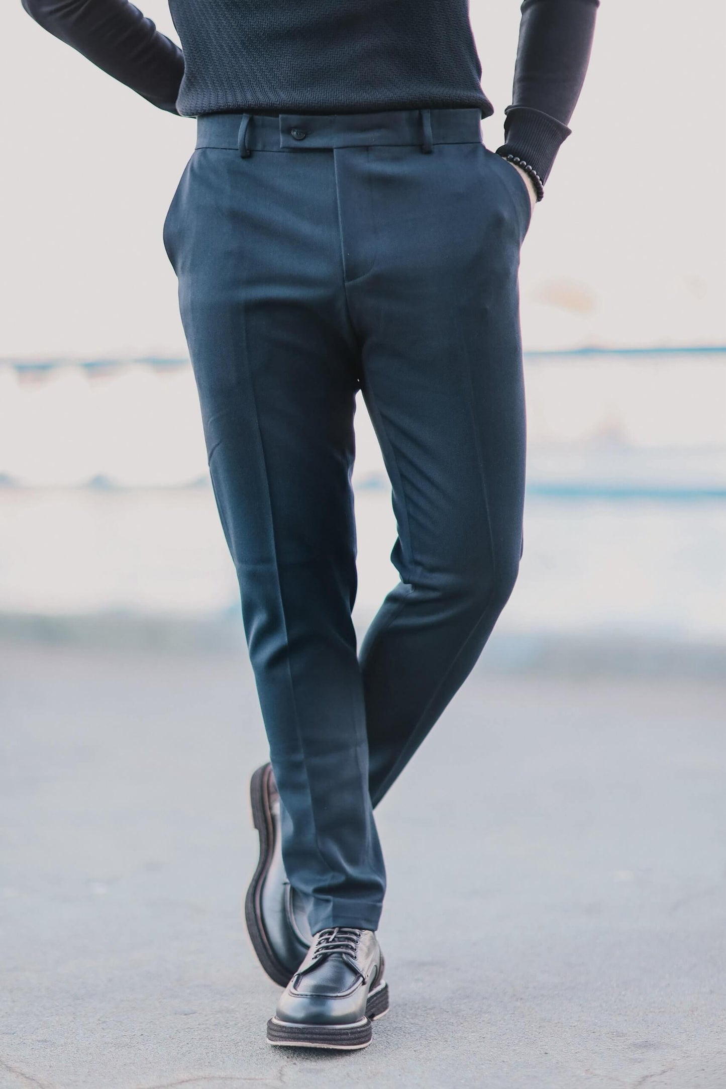 Men wearing navy blue slim-fit trousers paired with black derby shoes, standing outdoors in a clean minimalist urban setting.