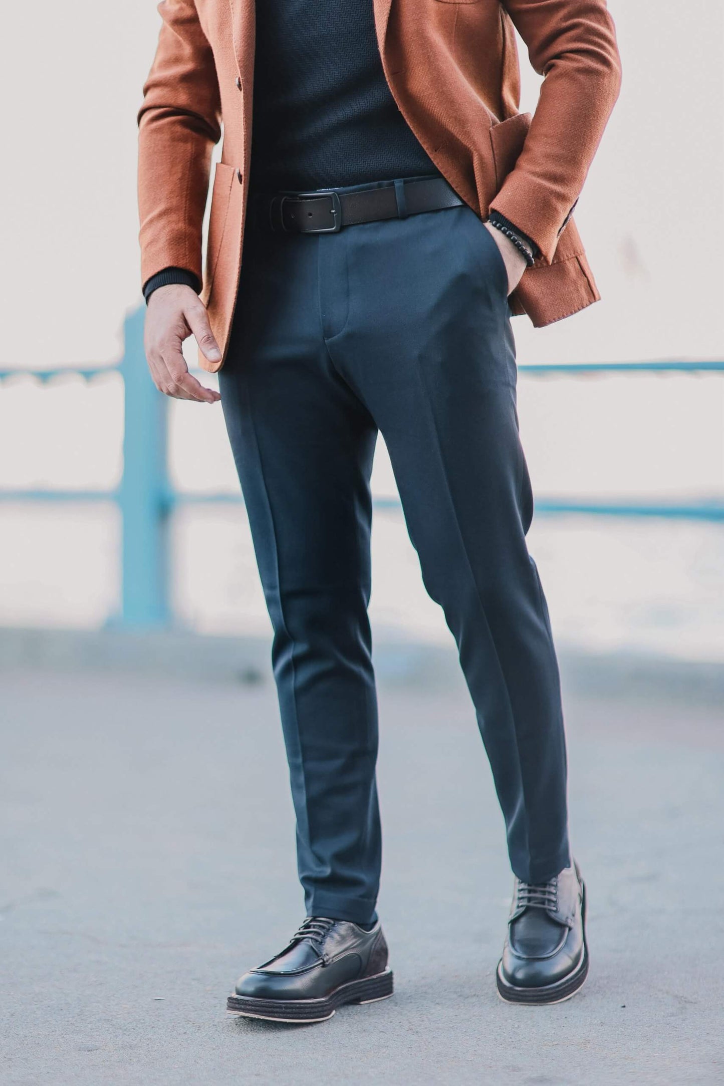 Men wearing navy blue slim-fit trousers paired with black derby shoes, standing outdoors in a clean minimalist urban setting.