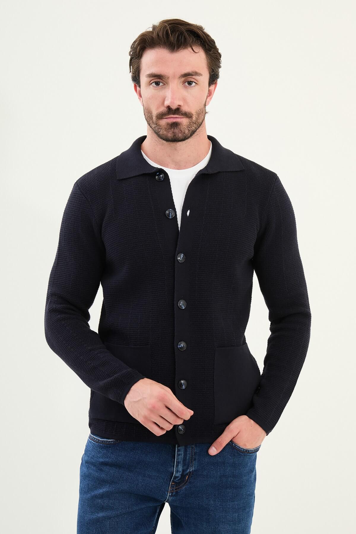 A man wearing a slim fit navy blue button-up cardigan with front pockets, styled with a white T-shirt and blue jeans.