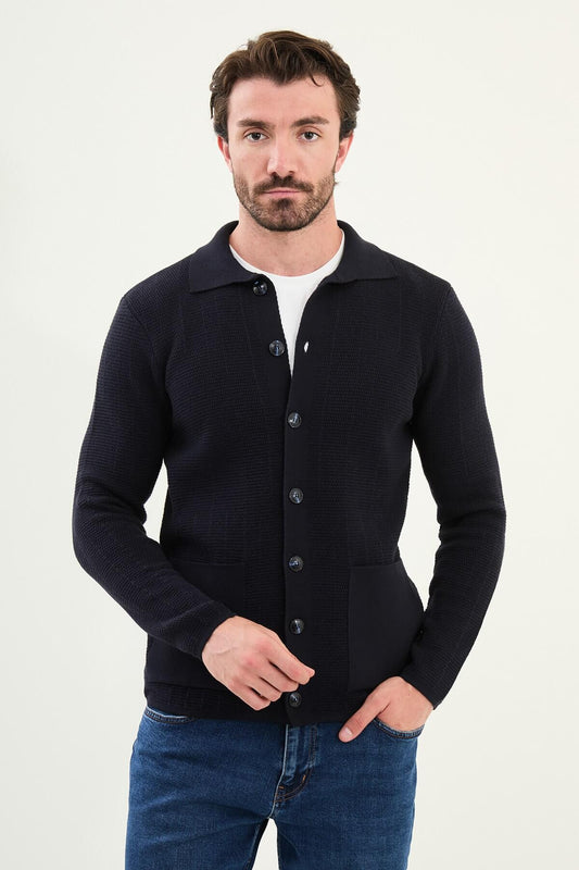A man wearing a slim fit navy blue button-up cardigan with front pockets, styled with a white T-shirt and blue jeans.