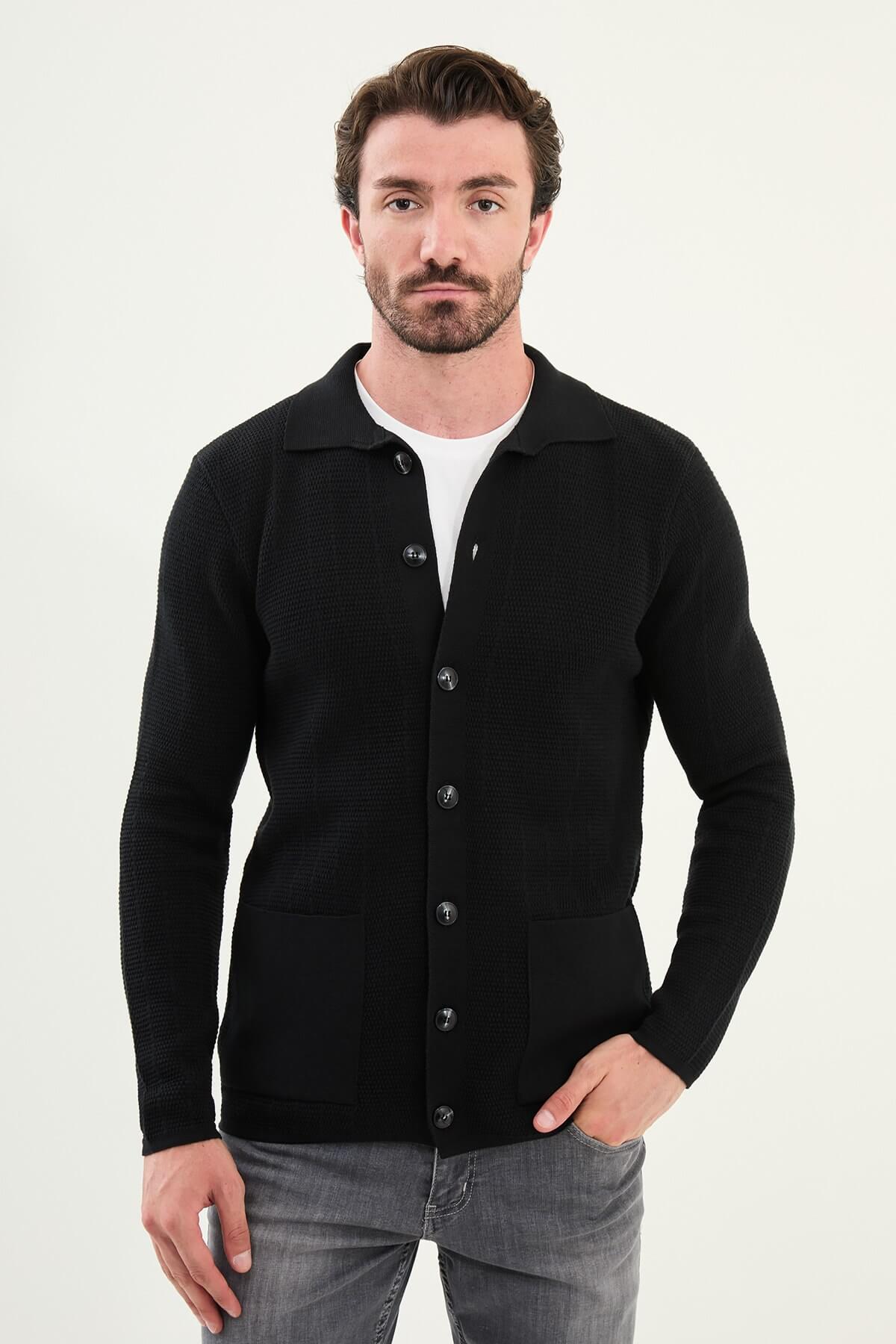 A man wearing a slim fit black button-up cardigan with front pockets, styled with a white T-shirt and grey jeans.