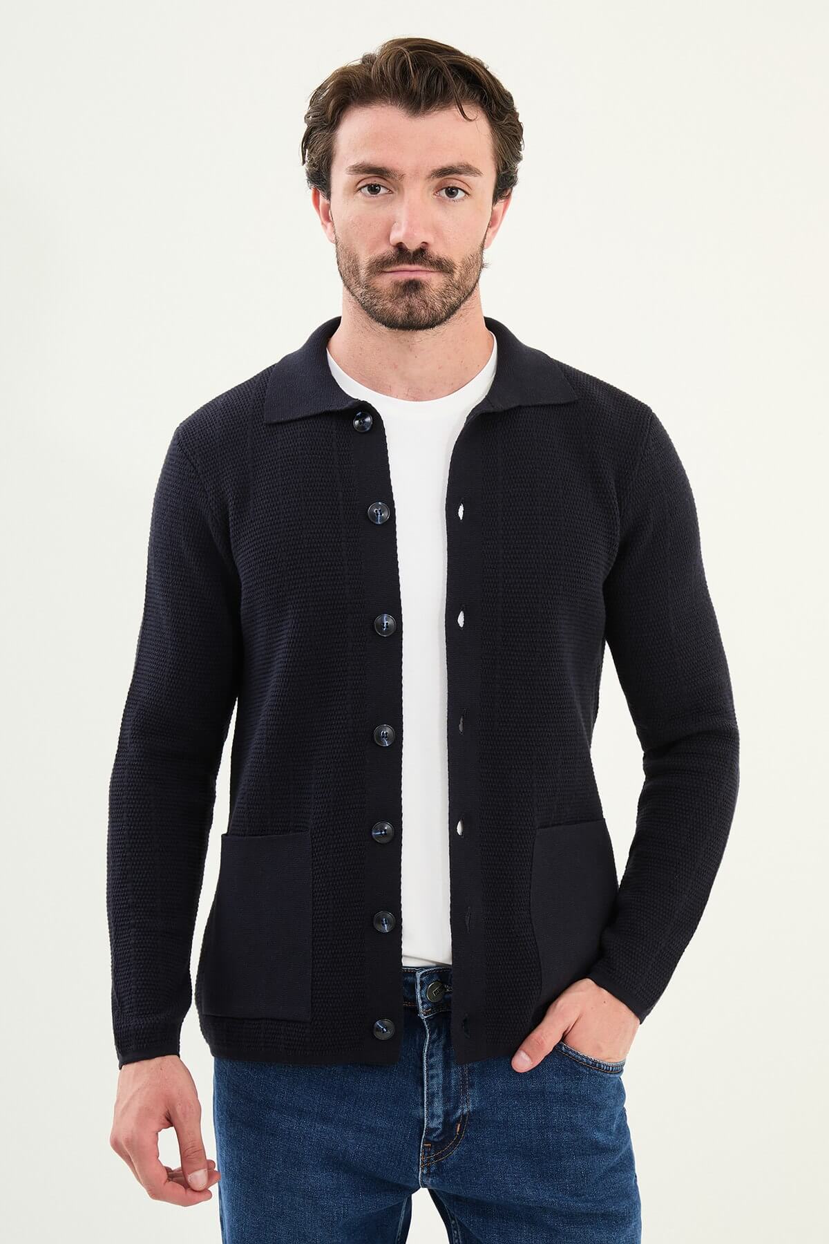 A man wearing a slim fit navy blue button-up cardigan with front pockets, styled with a white T-shirt and blue jeans.