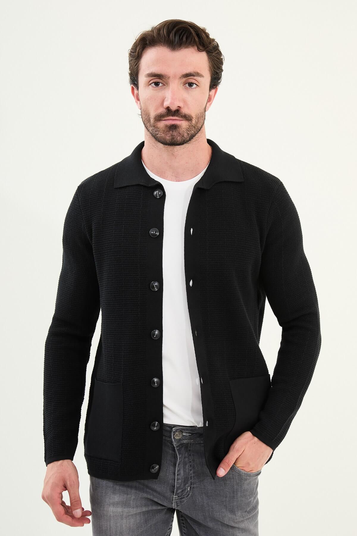 A man wearing a slim fit black button-up cardigan with front pockets, styled with a white T-shirt and grey jeans.