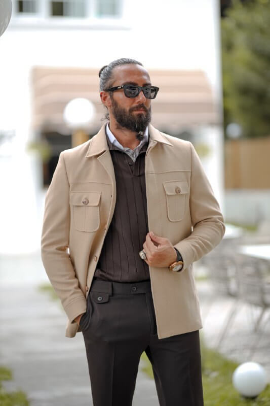 Man wearing a beige slim fit short jacket with pocket details, styled over a dark knit sweater and tailored trousers.
