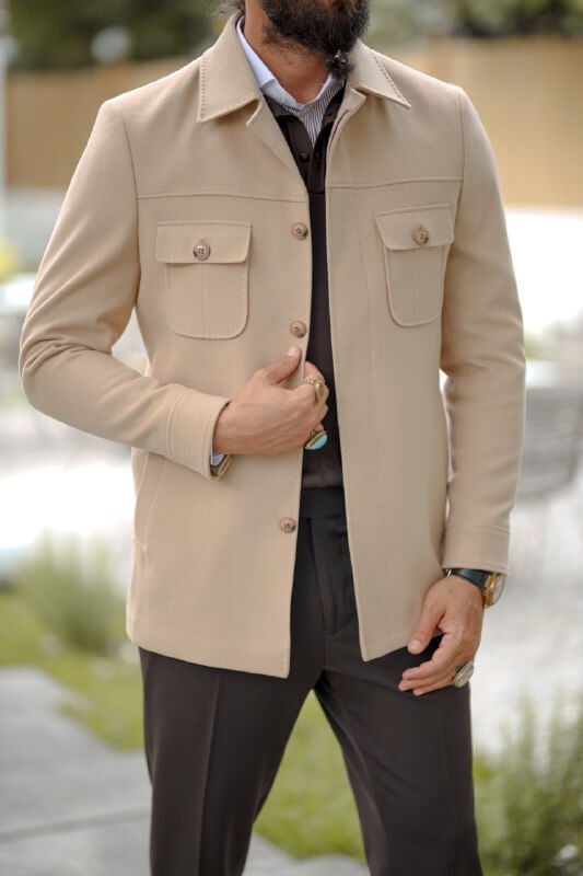 Man wearing a beige slim fit short jacket with pocket details, styled over a dark knit sweater and tailored trousers.