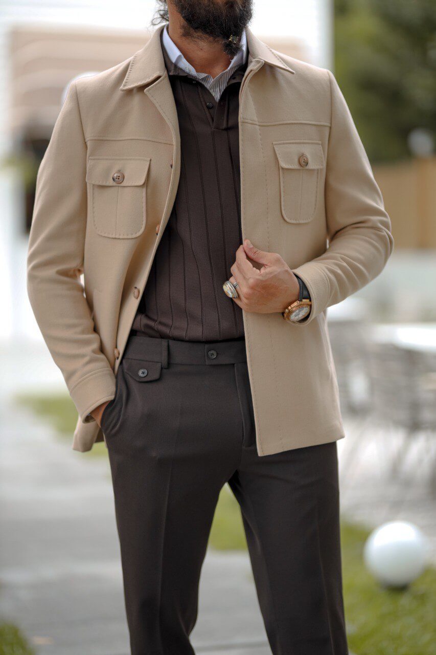 Man wearing a beige slim fit short jacket with pocket details, styled over a dark knit sweater and tailored trousers.
