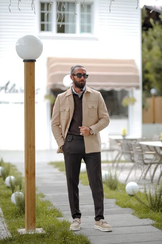 Man wearing a beige slim fit short jacket with pocket details, styled over a dark knit sweater and tailored trousers.