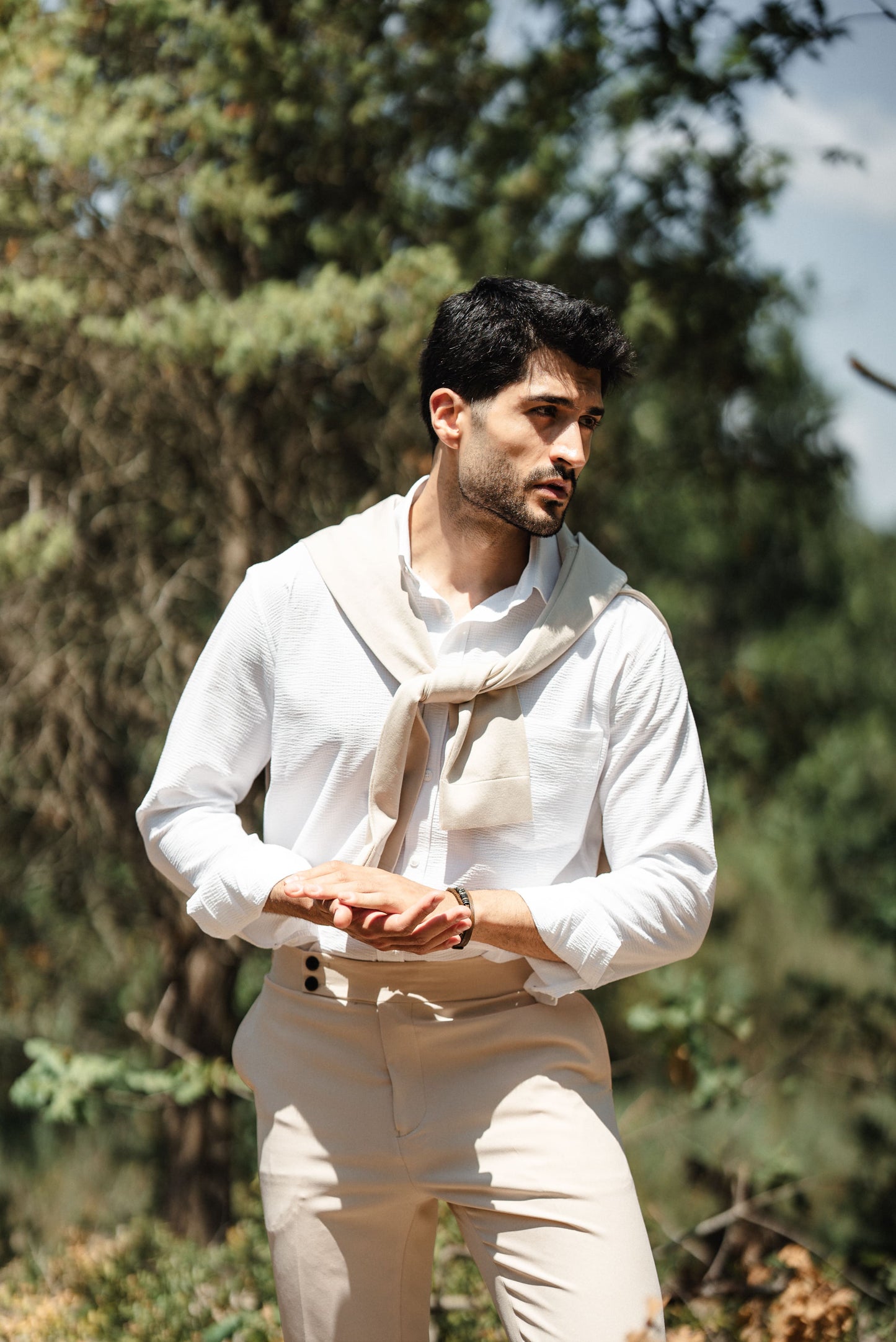 HolloMen Beige Linen Shirt worn by a man with a beige sweater draped over his shoulder, standing in a lush, natural outdoor setting.