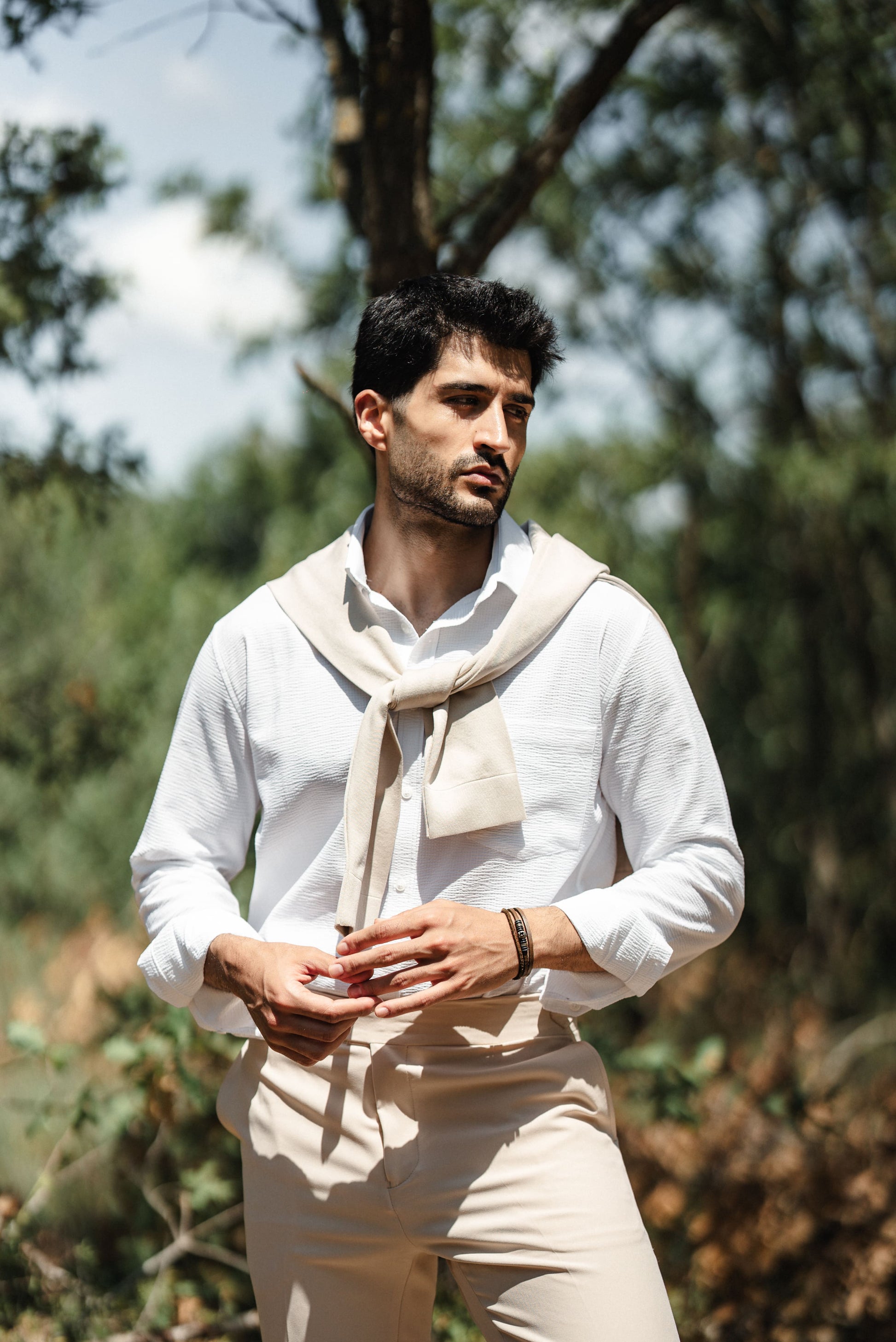 HolloMen Beige Linen Shirt worn by a man with a beige sweater draped over his shoulder, standing in a lush, natural outdoor setting.