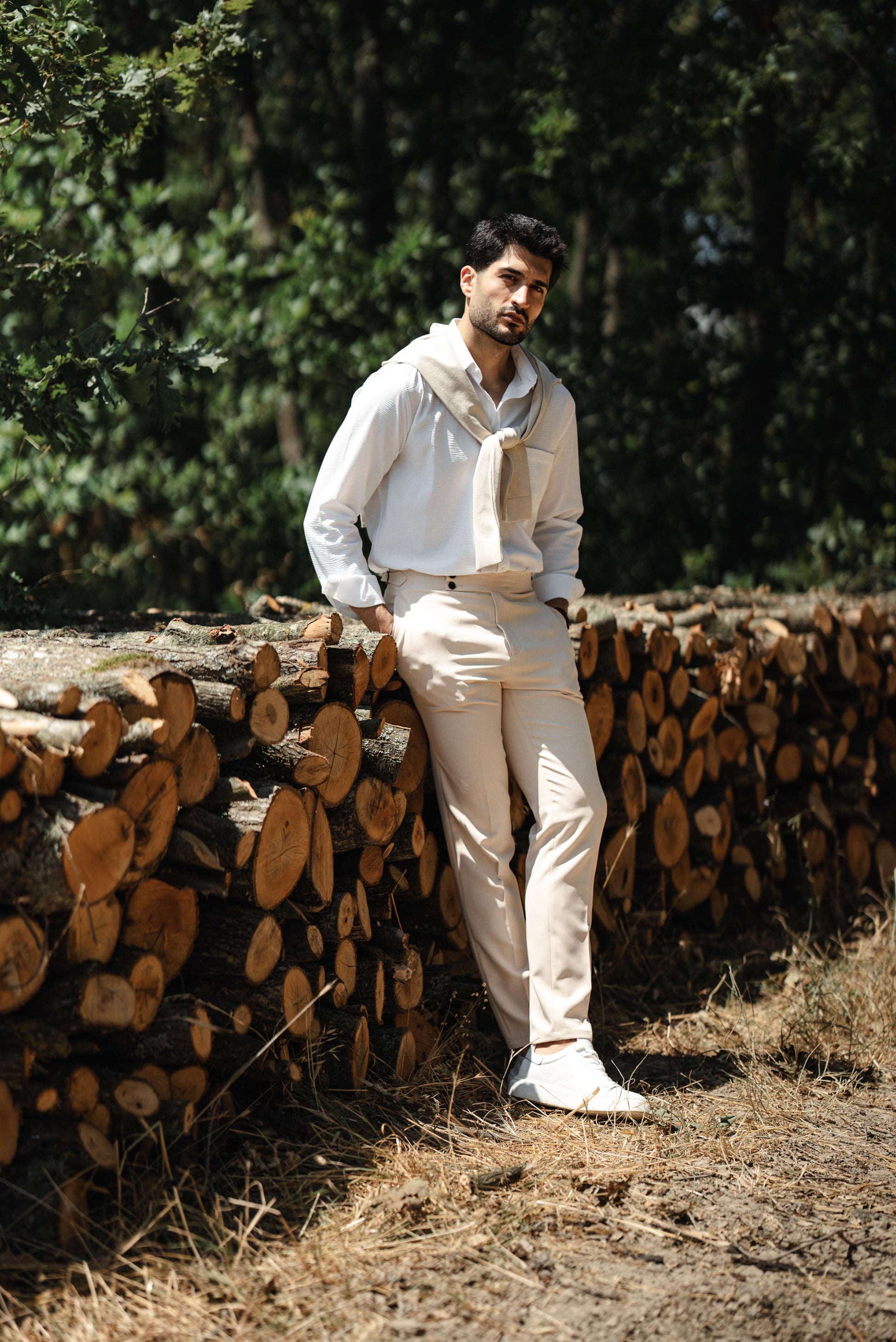 HolloMen Beige Linen Shirt worn by a man with a beige sweater draped over his shoulder, standing in a lush, natural outdoor setting.