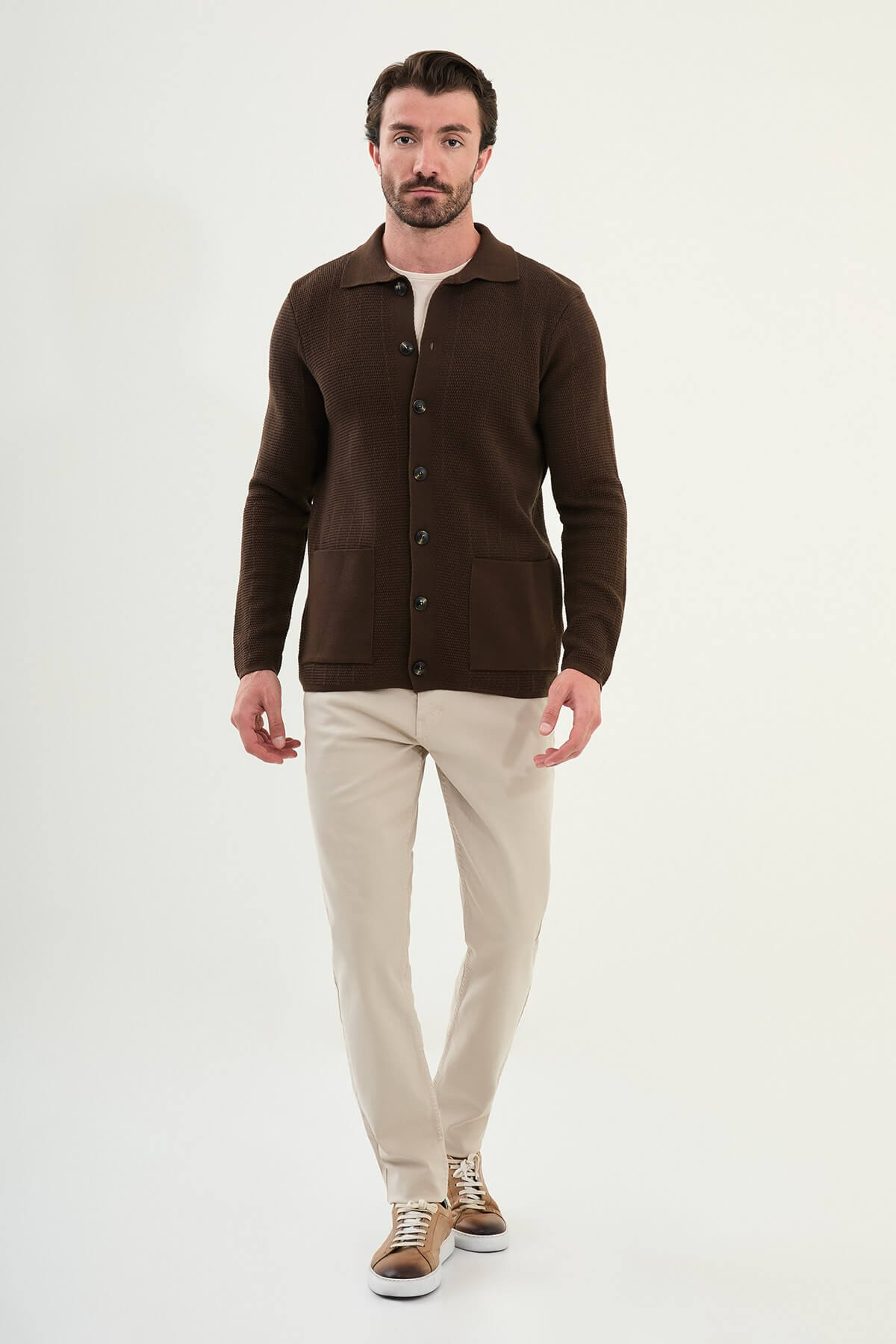 A man wearing a brown slim fit button-up cardigan with front pockets, paired with beige chinos and brown sneakers.