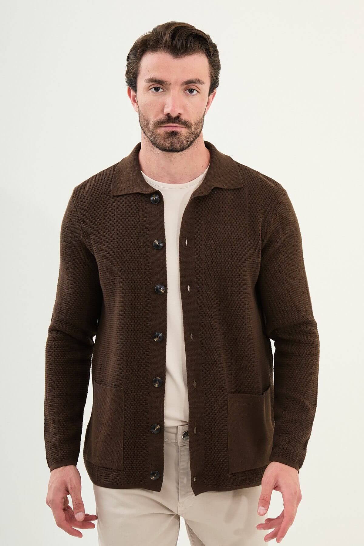 A man wearing a brown slim fit button-up cardigan with front pockets, paired with beige chinos and brown sneakers.