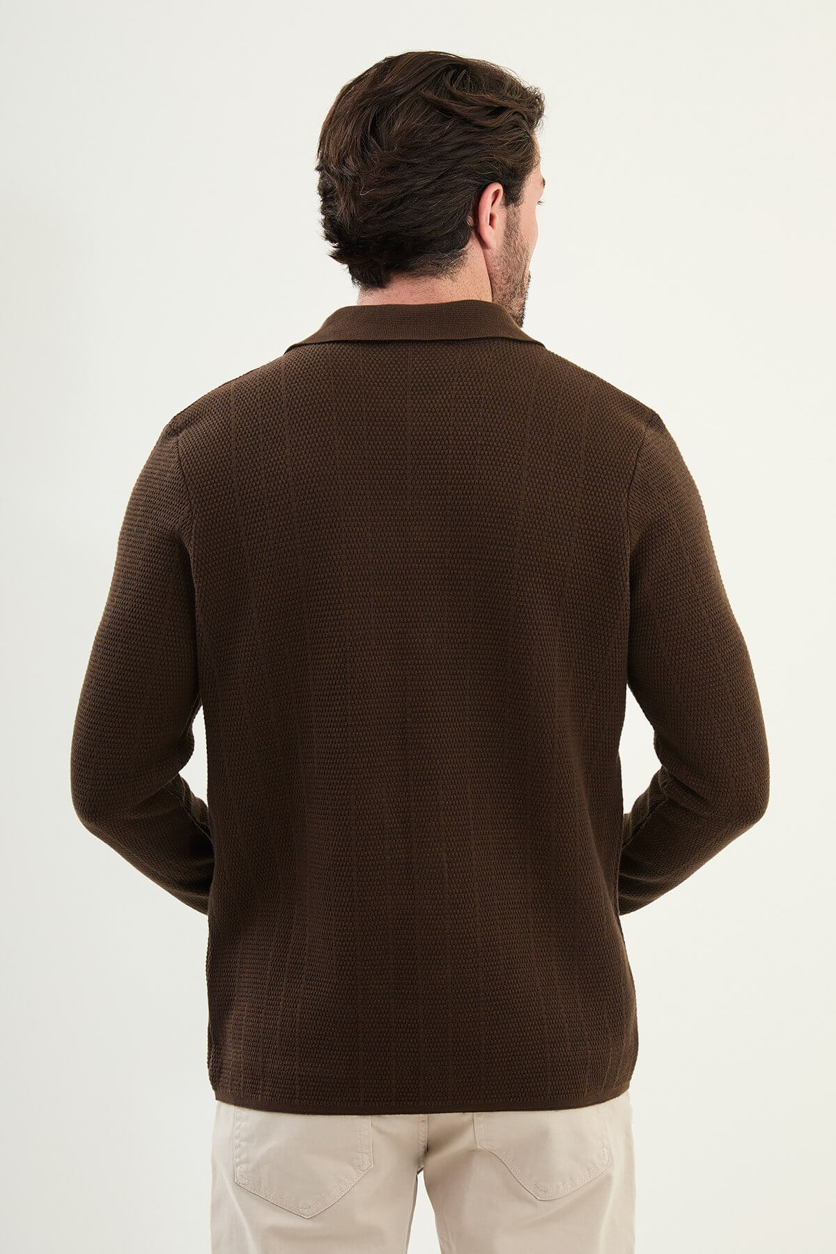 A man wearing a brown slim fit button-up cardigan with front pockets, paired with beige chinos and brown sneakers.