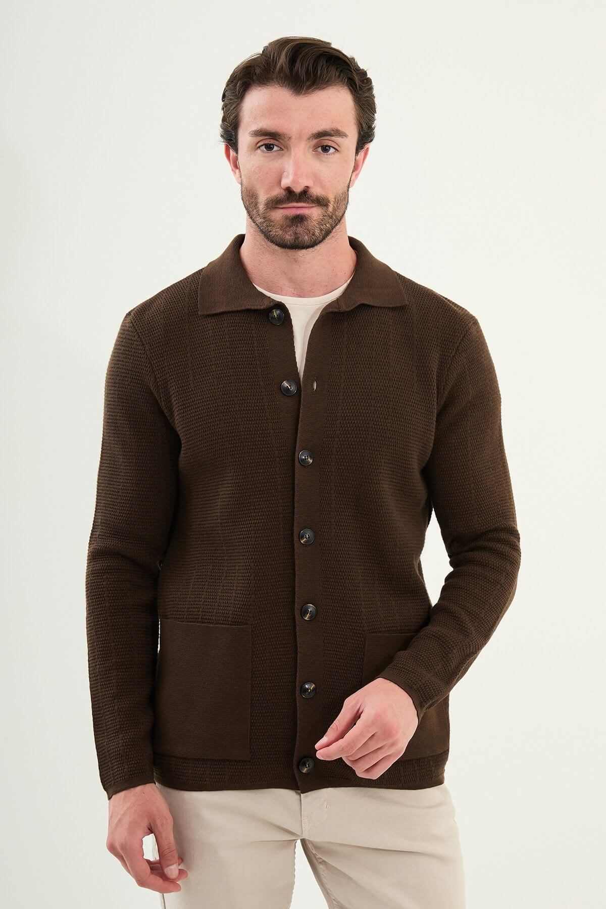 A man wearing a brown slim fit button-up cardigan with front pockets, paired with beige chinos and brown sneakers.