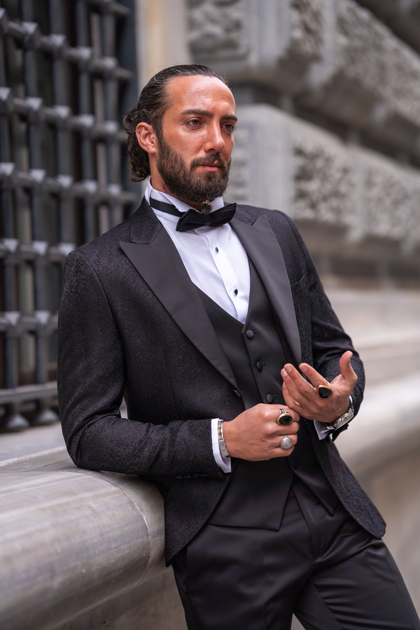 Slim-fit black tuxedo with double-button closure and pointed collar, modeled for fall-winter weddings and formal events — styled with matching vest, shirt, tie, and tailored trousers.