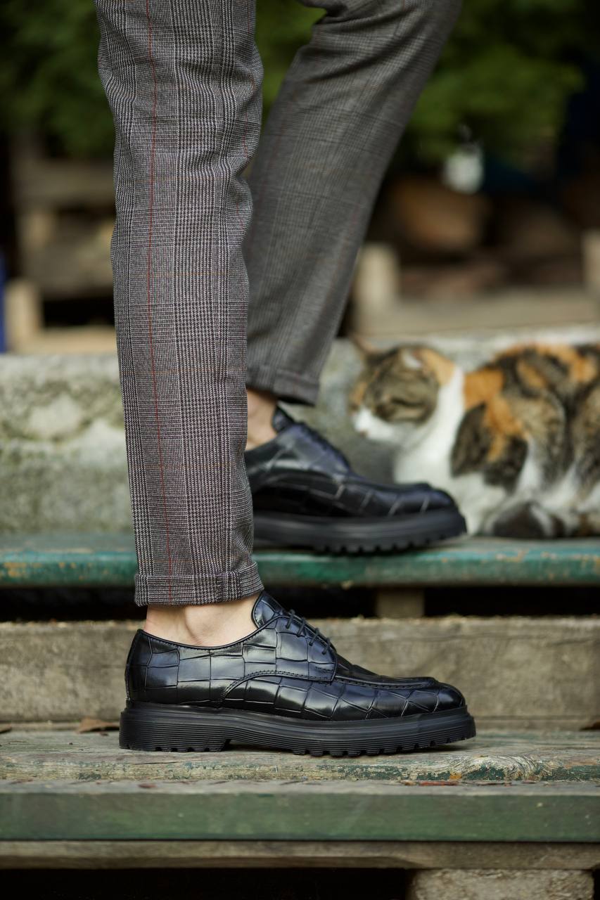 Black croc-embossed leather derby shoes with EVA sole, worn with tailored grey check trousers. 