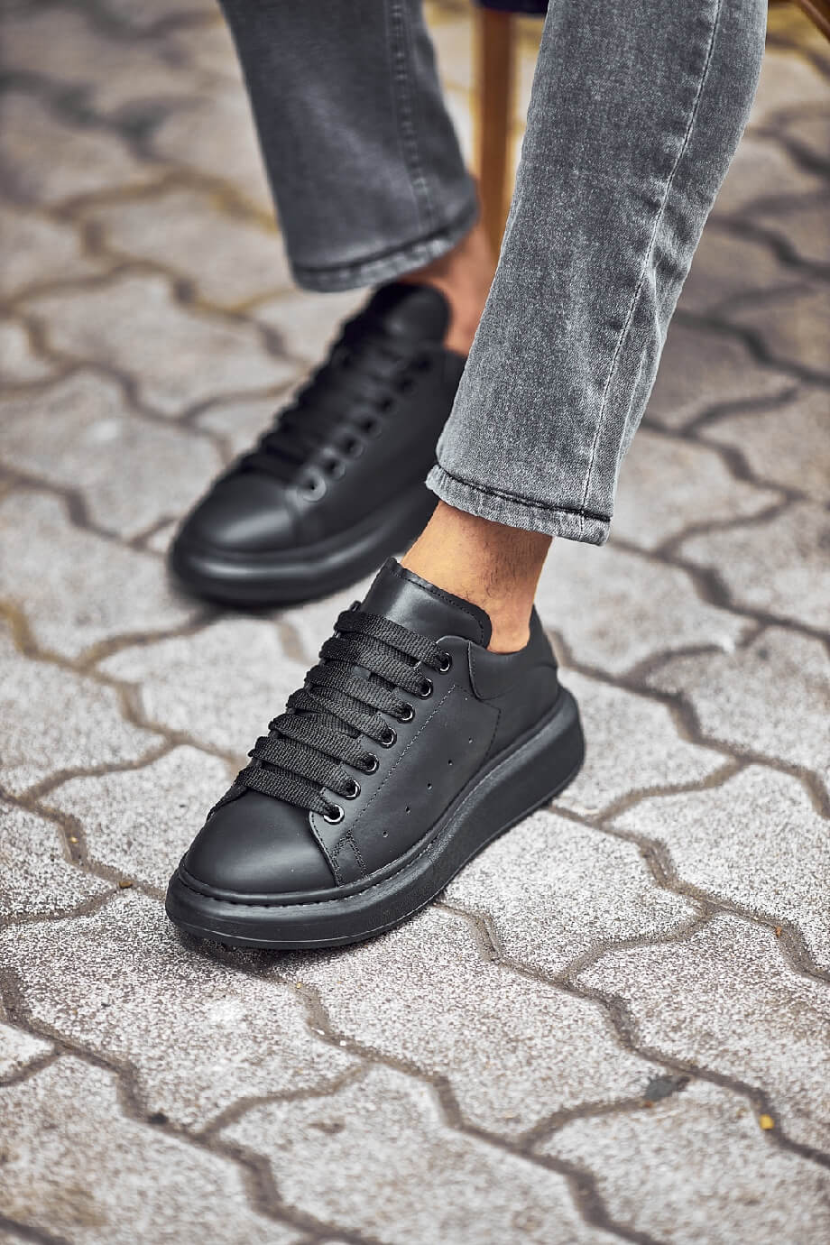 Black leather sneakers with a full black sole, styled with fitted grey jeans