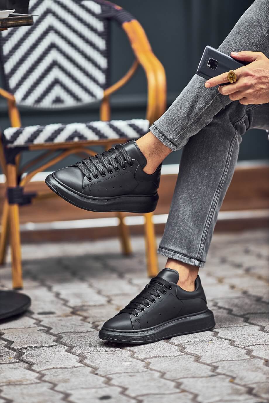 Black leather sneakers with a full black sole, styled with fitted grey jeans