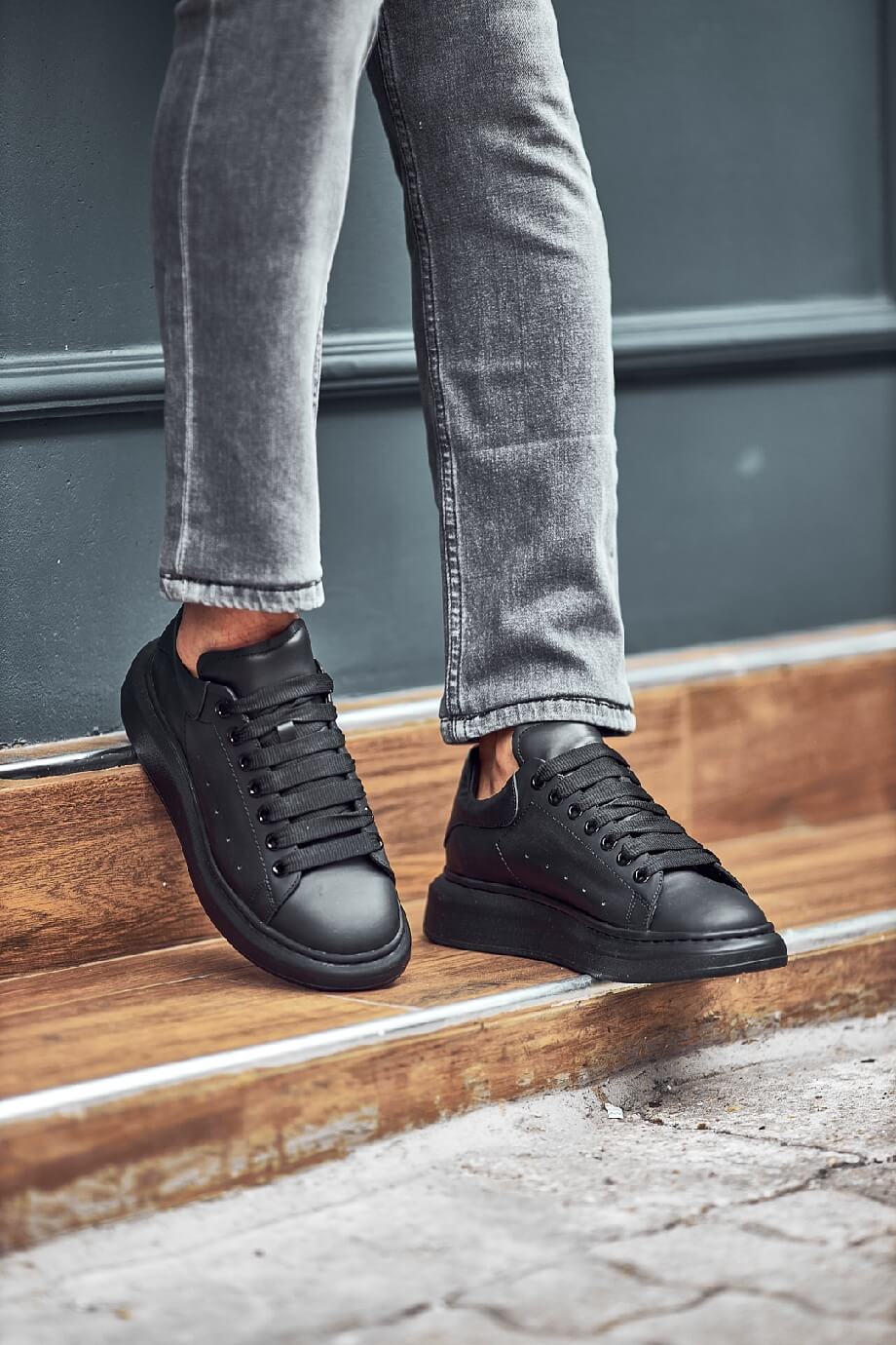 Black leather sneakers with a full black sole, styled with fitted grey jeans