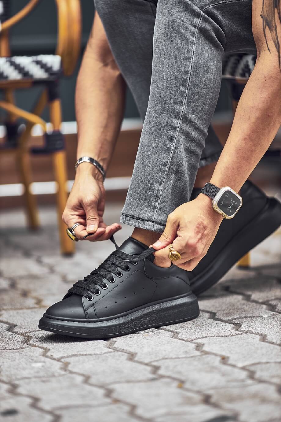 Black leather sneakers with a full black sole, styled with fitted grey jeans