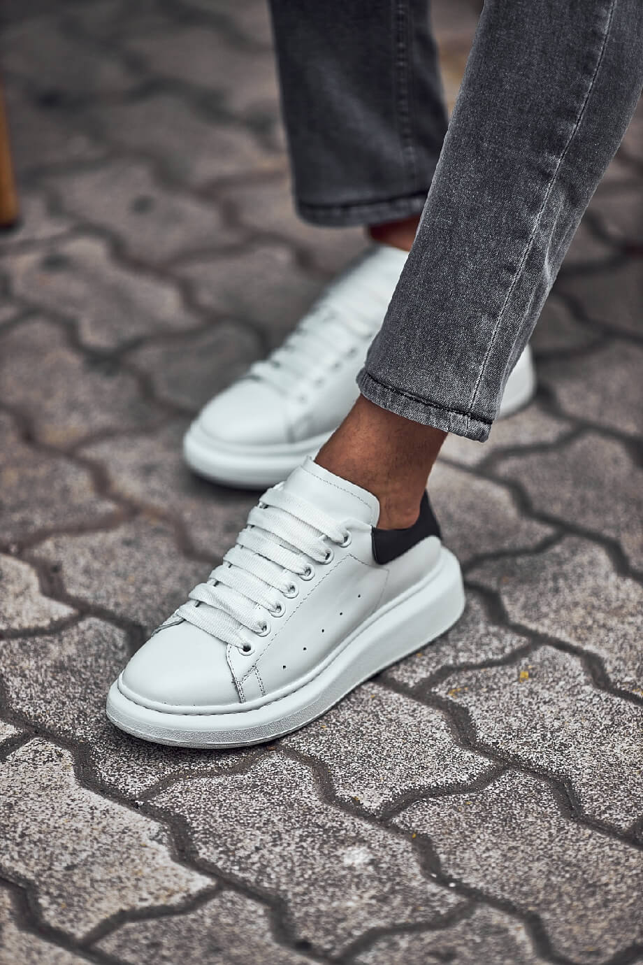 White leather sneakers with black heel detail worn with grey jeans