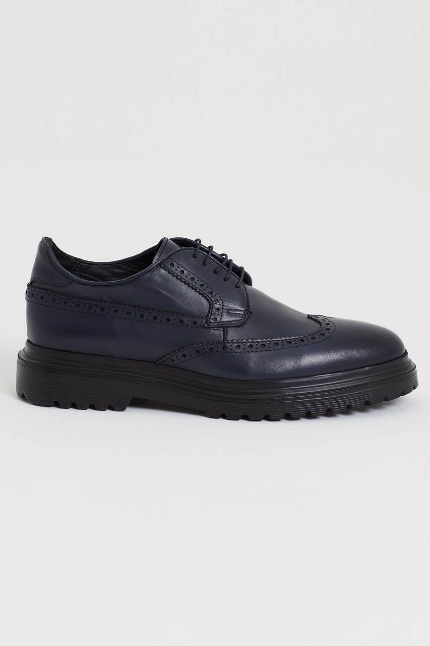 Navy blue leather brogue shoe with intricate perforation details, featuring a chunky black sole, displayed against a minimalist light background.