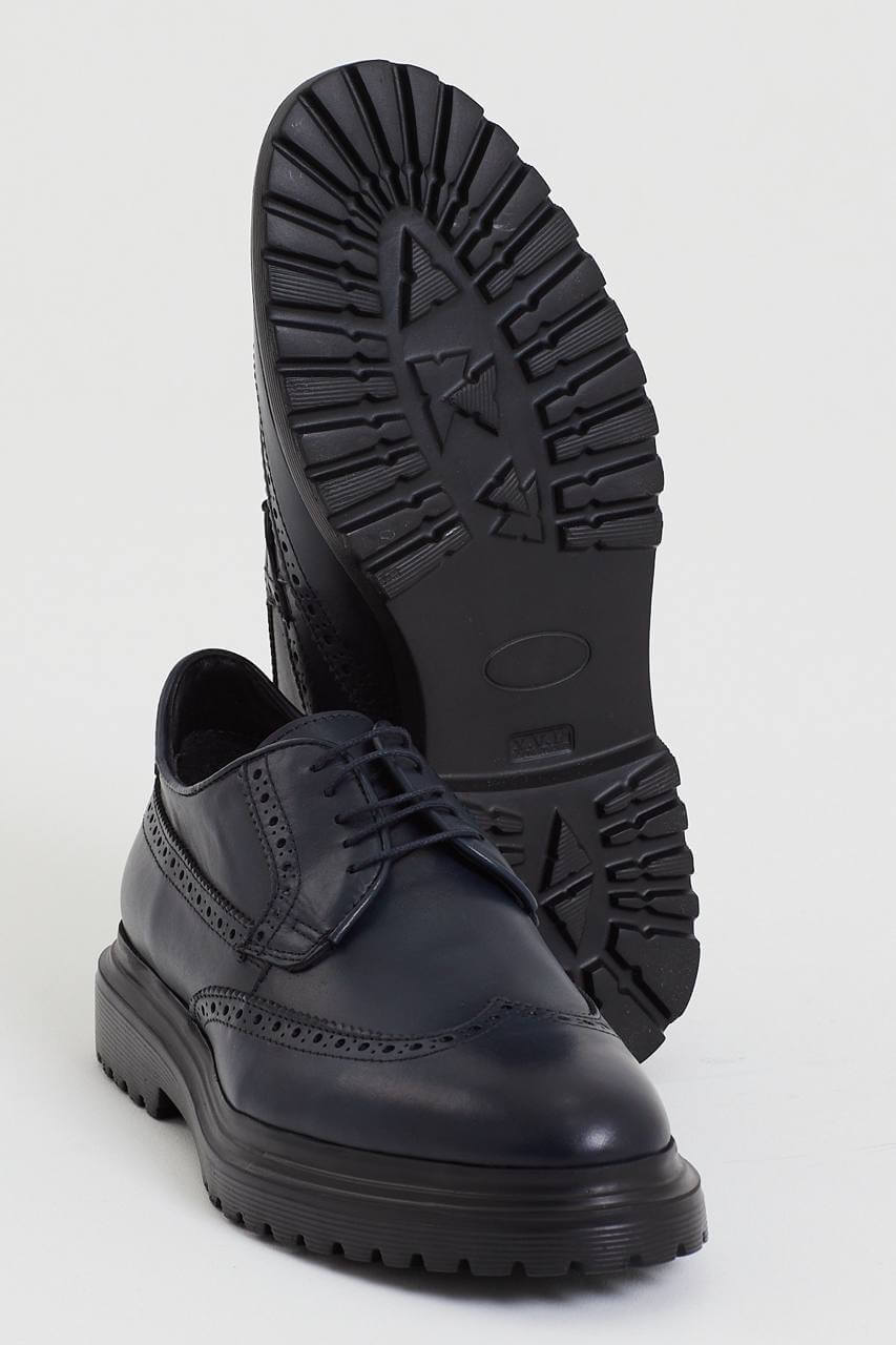 Navy blue leather brogue shoe with intricate perforation details, featuring a chunky black sole, displayed against a minimalist light background.