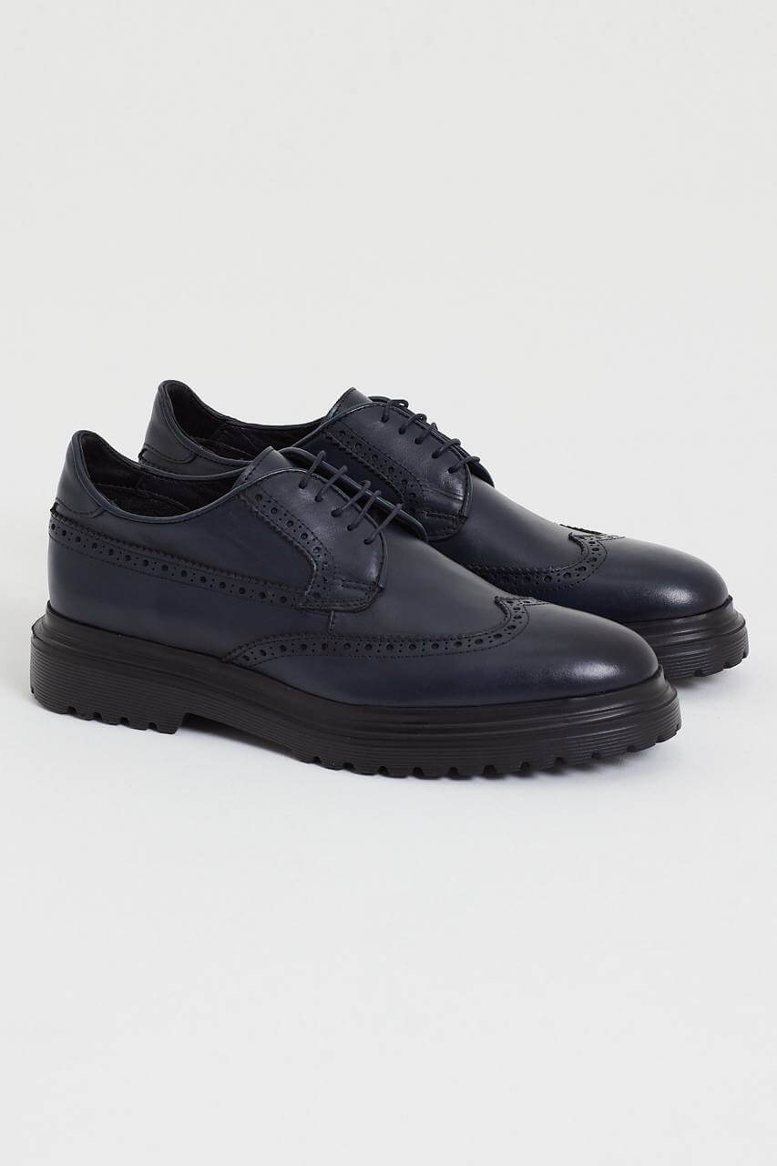 Navy blue leather brogue shoe with intricate perforation details, featuring a chunky black sole, displayed against a minimalist light background.