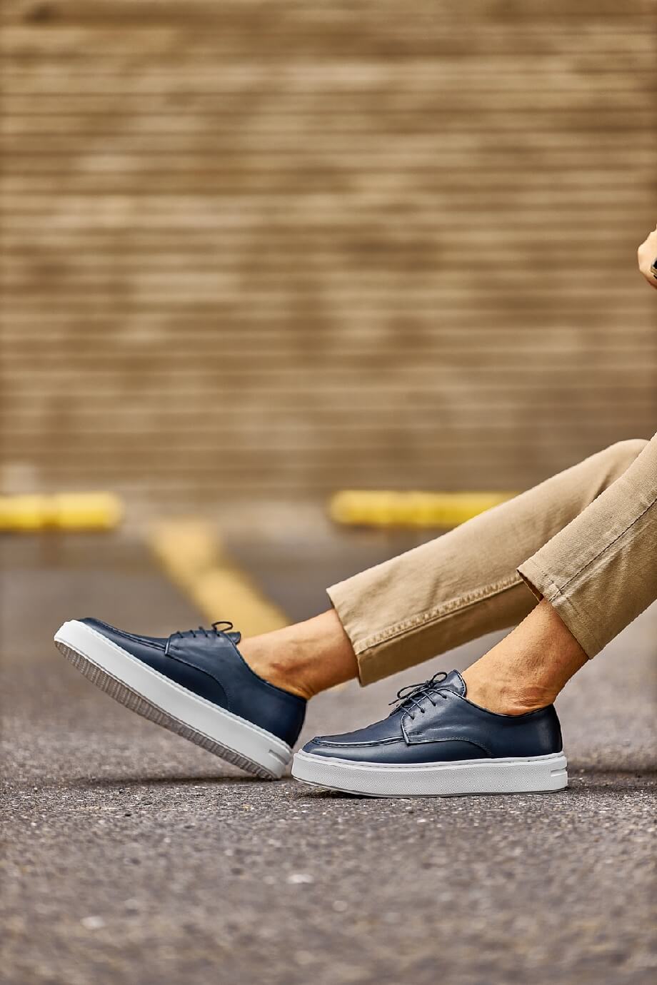Close-up of a man walking in Tulum navy leather lace-up derby shoes with white EVA soles, styled with cropped khaki trousers on a sunlit street.
