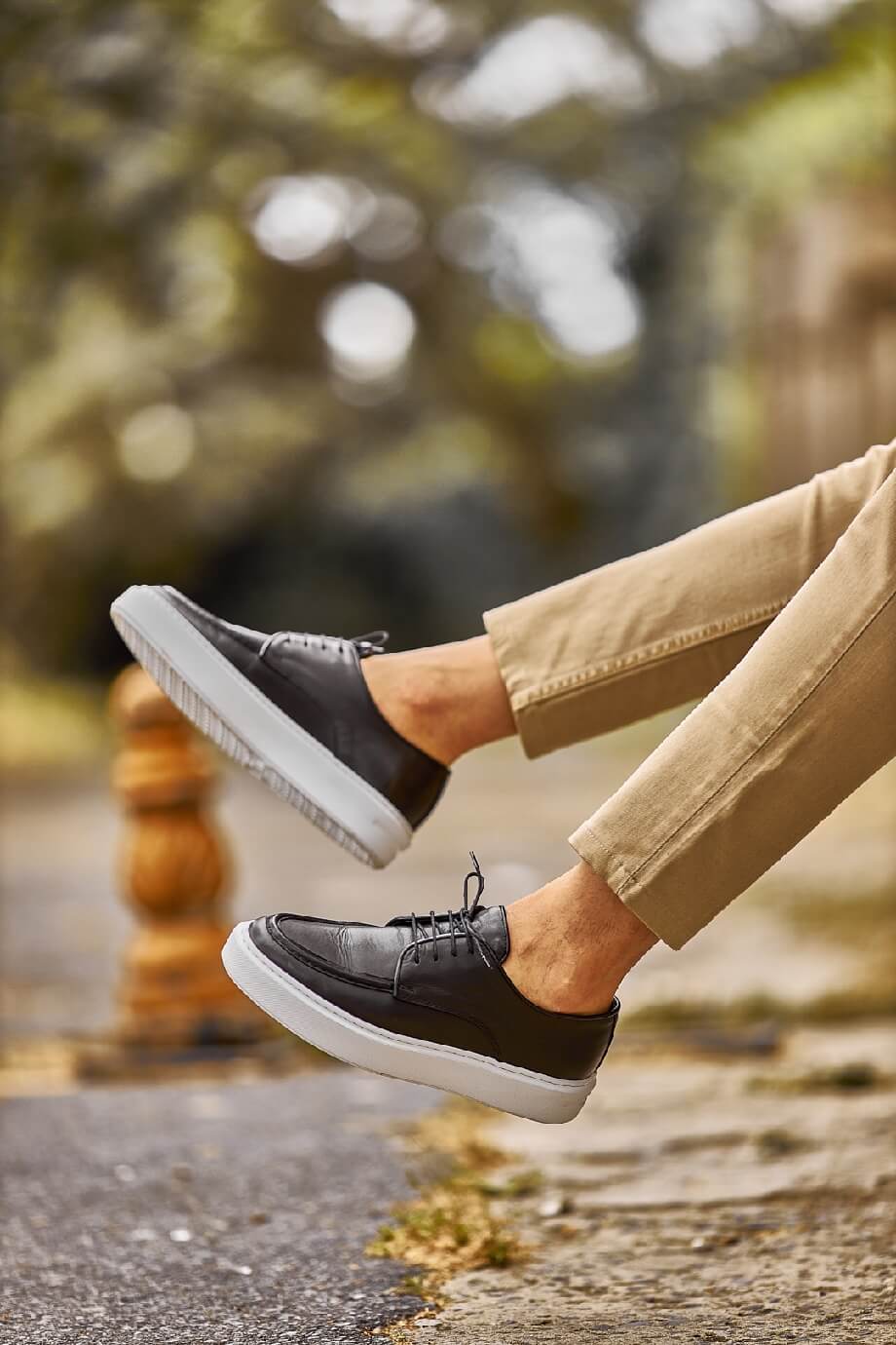 Close-up of a man walking in Tulum navy leather lace-up derby shoes with white EVA soles, styled with cropped khaki trousers on a sunlit street.