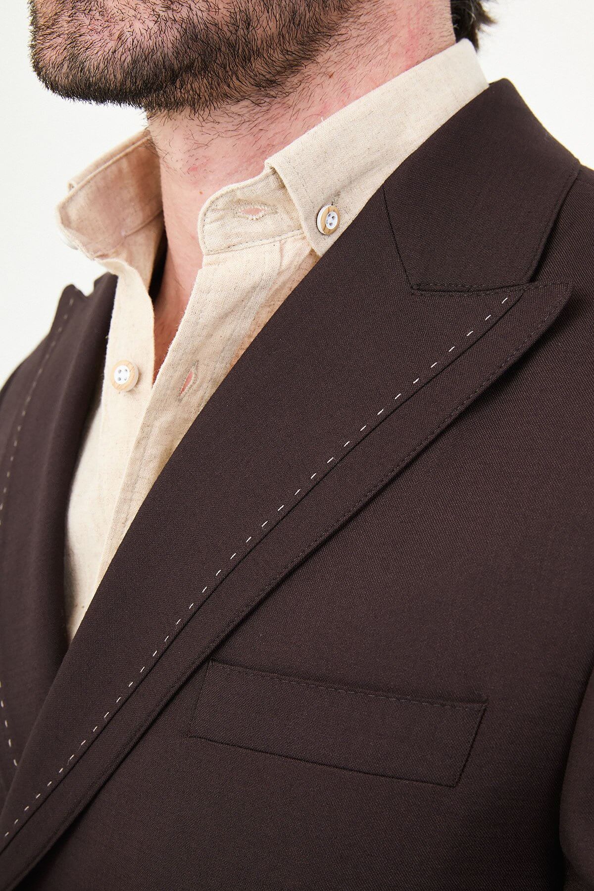 a brown slim-fit double-breasted linen-blend suit with peak lapels, contrast pick stitching, matching trousers, and an open-collar cream shirt.