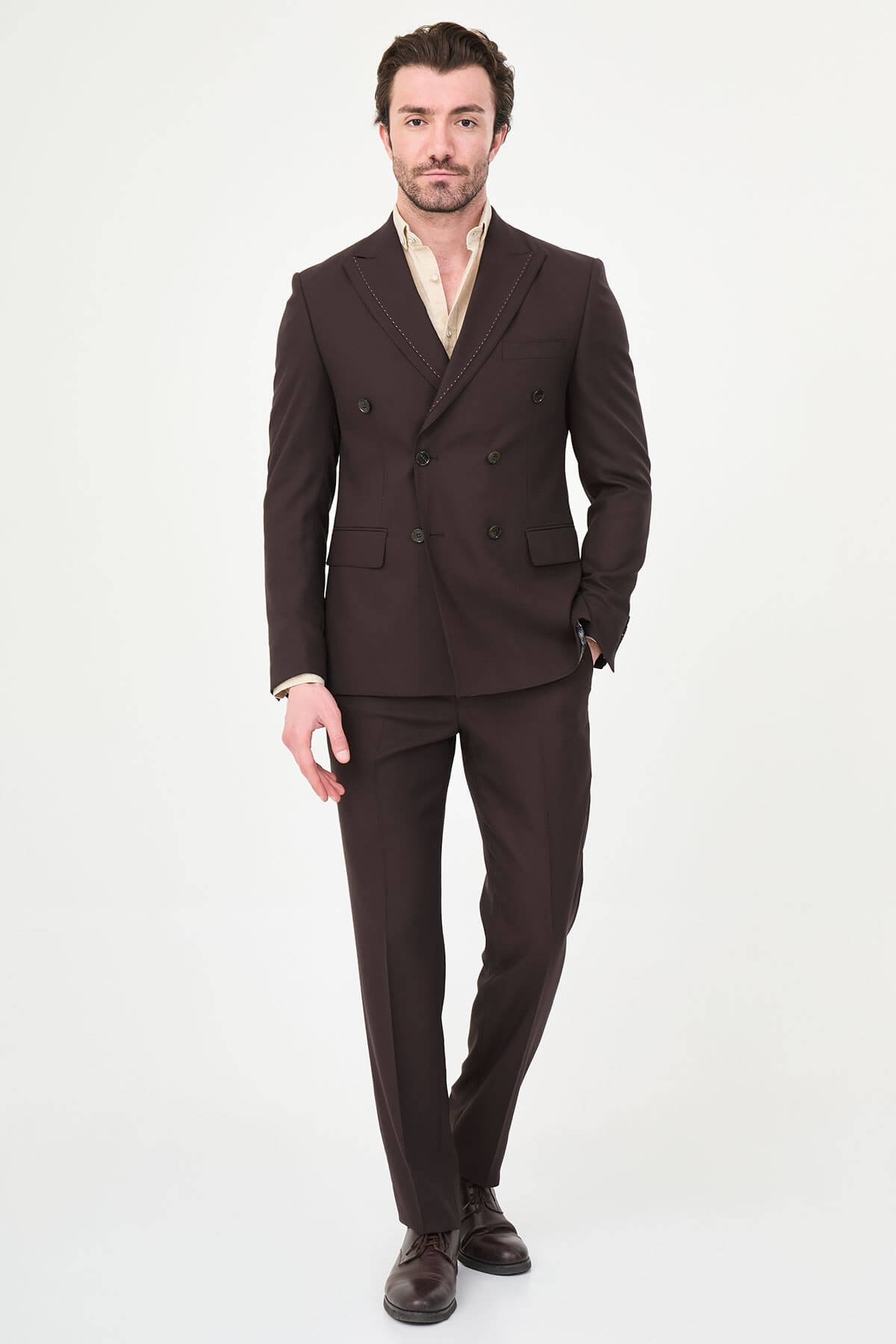 a brown slim-fit double-breasted linen-blend suit with peak lapels, contrast pick stitching, matching trousers, and an open-collar cream shirt.