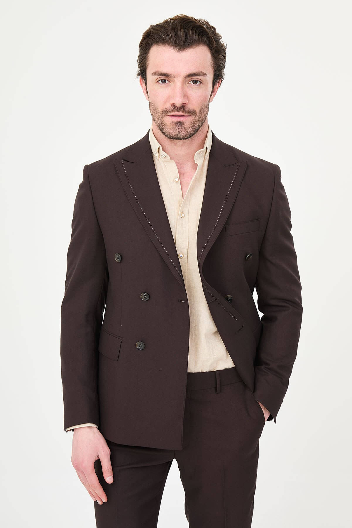 a brown slim-fit double-breasted linen-blend suit with peak lapels, contrast pick stitching, matching trousers, and an open-collar cream shirt.
