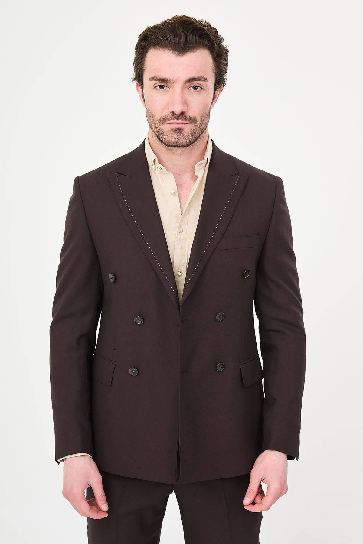 a brown slim-fit double-breasted linen-blend suit with peak lapels, contrast pick stitching, matching trousers, and an open-collar cream shirt.