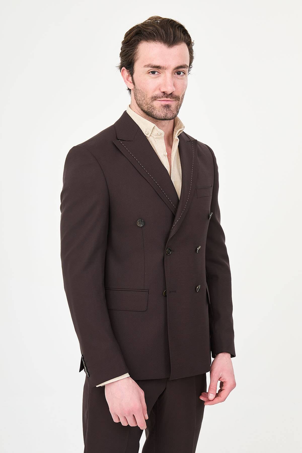 a brown slim-fit double-breasted linen-blend suit with peak lapels, contrast pick stitching, matching trousers, and an open-collar cream shirt.