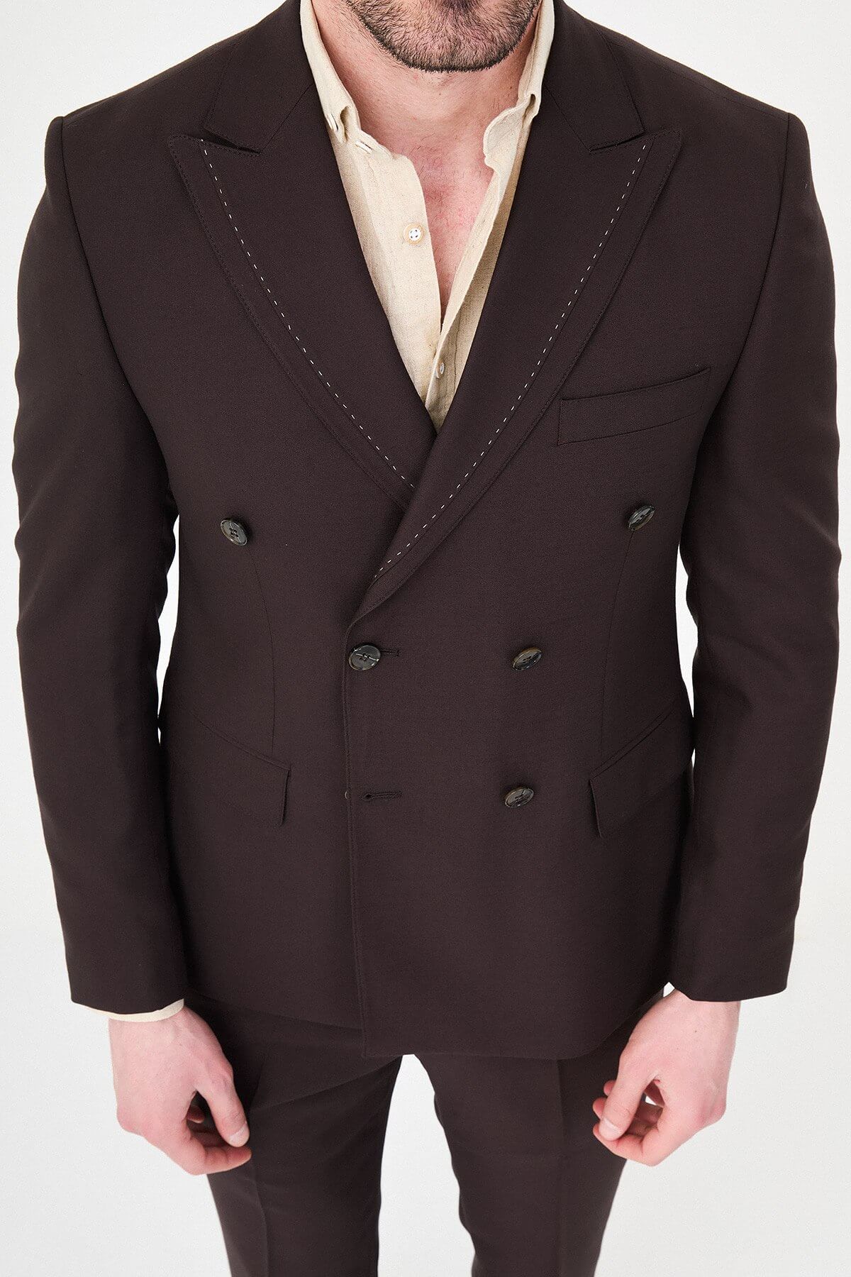 a brown slim-fit double-breasted linen-blend suit with peak lapels, contrast pick stitching, matching trousers, and an open-collar cream shirt.
