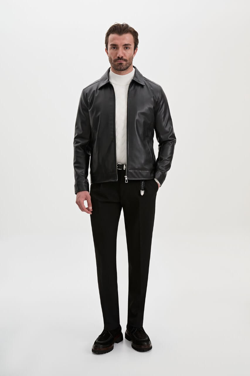 Men's black leather-look jacket styled with a cream knit sweater and black trousers.