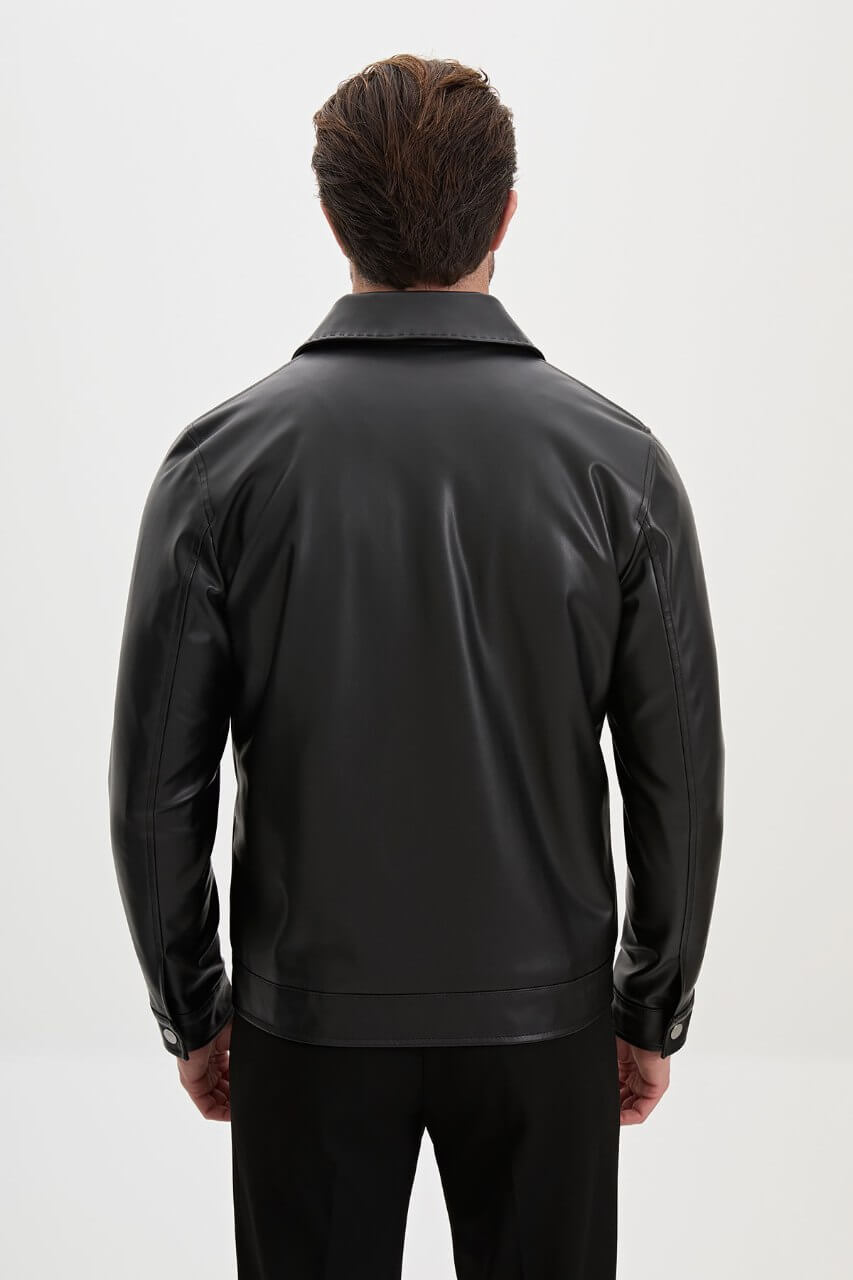 Men's black leather-look jacket styled with a cream knit sweater and black trousers.