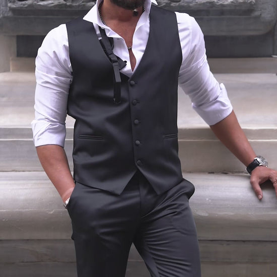 Slim-fit black tuxedo with double-button closure and pointed collar, modeled for fall-winter weddings and formal events — styled with matching vest, shirt, tie, and tailored trousers.