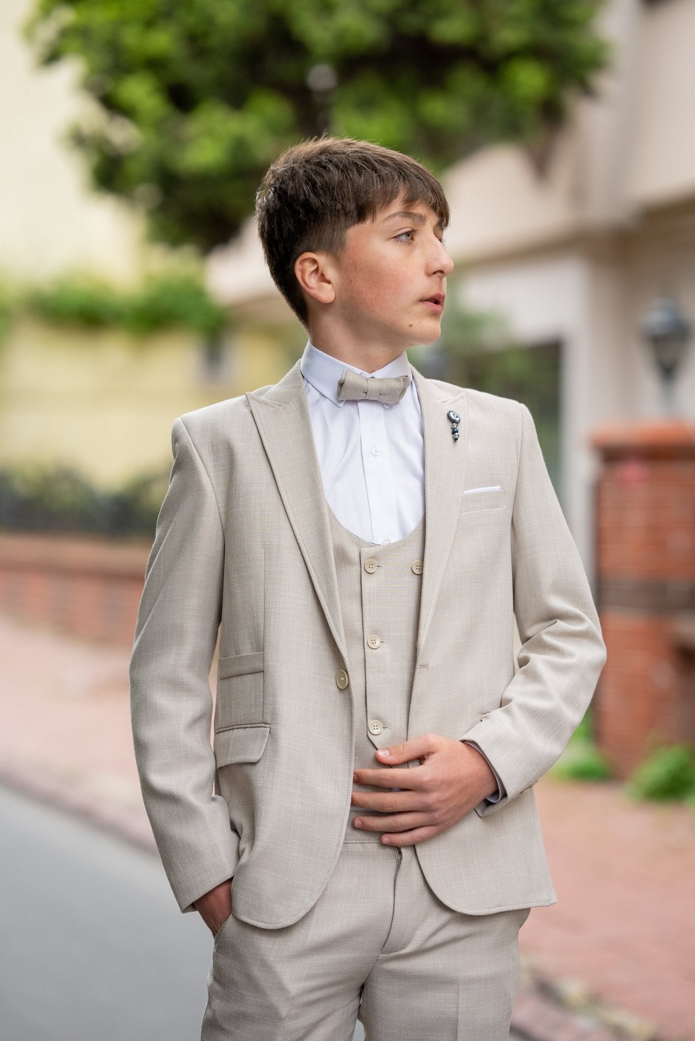 Father and his two sons walking down a street in matching beige tuxedos with elegant bow ties, exuding confidence and style during a formal occasion.