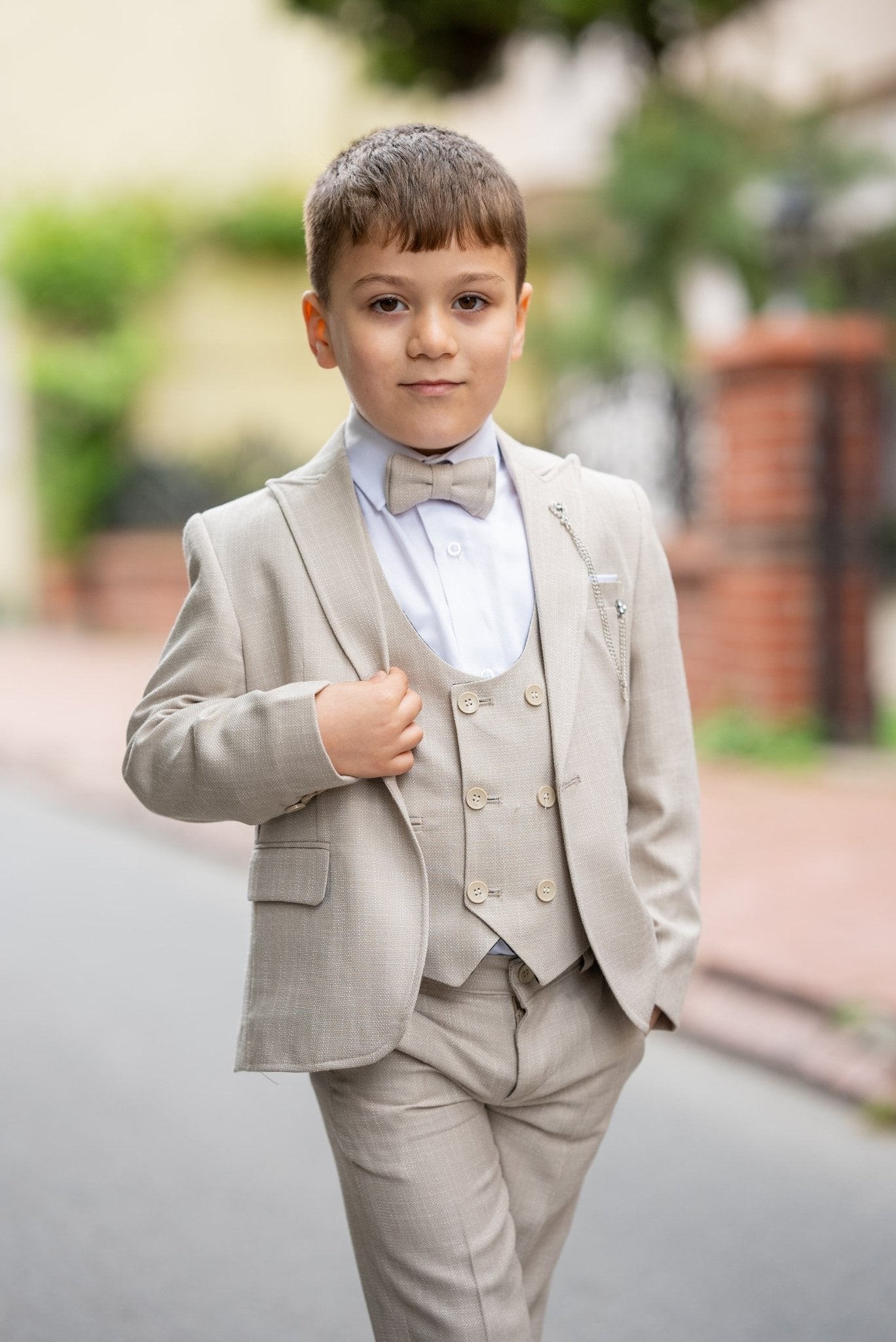Father and his two sons walking down a street in matching beige tuxedos with elegant bow ties, exuding confidence and style during a formal occasion.