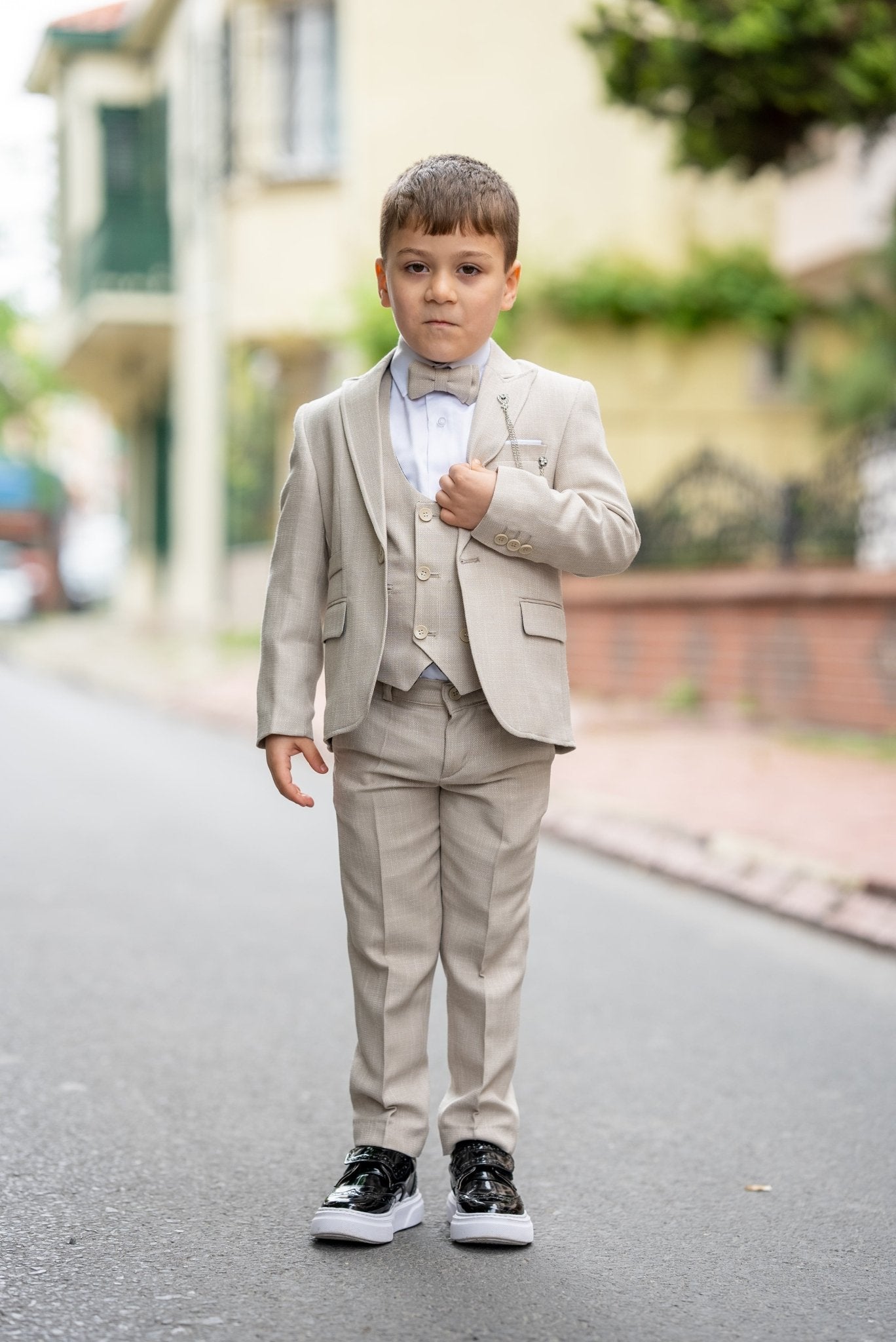 Father and his two sons walking down a street in matching beige tuxedos with elegant bow ties, exuding confidence and style during a formal occasion.