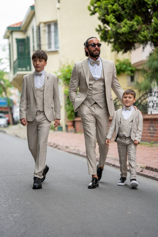 Father and his two sons walking down a street in matching beige tuxedos with elegant bow ties, exuding confidence and style during a formal occasion.