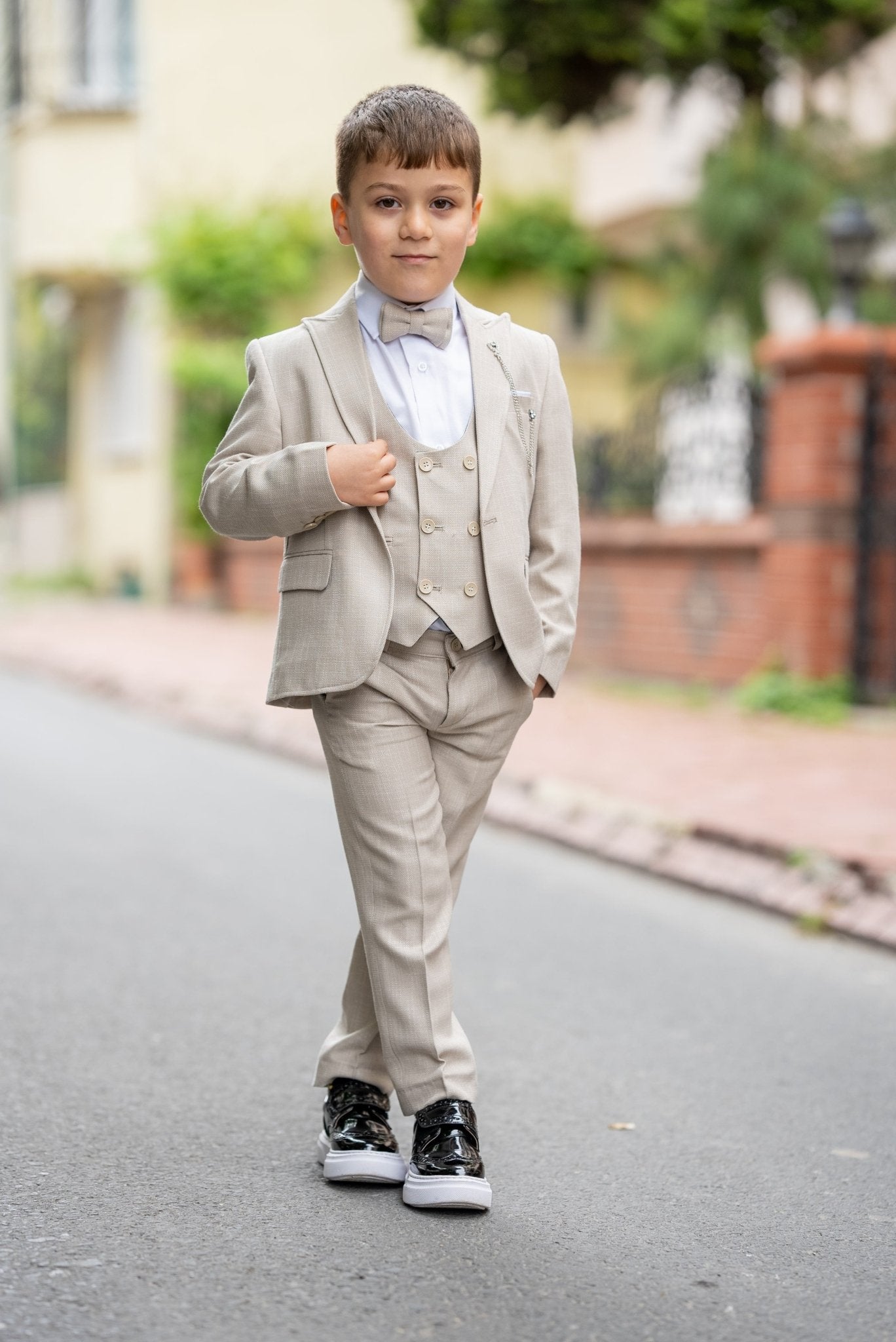 Father and his two sons walking down a street in matching beige tuxedos with elegant bow ties, exuding confidence and style during a formal occasion.
