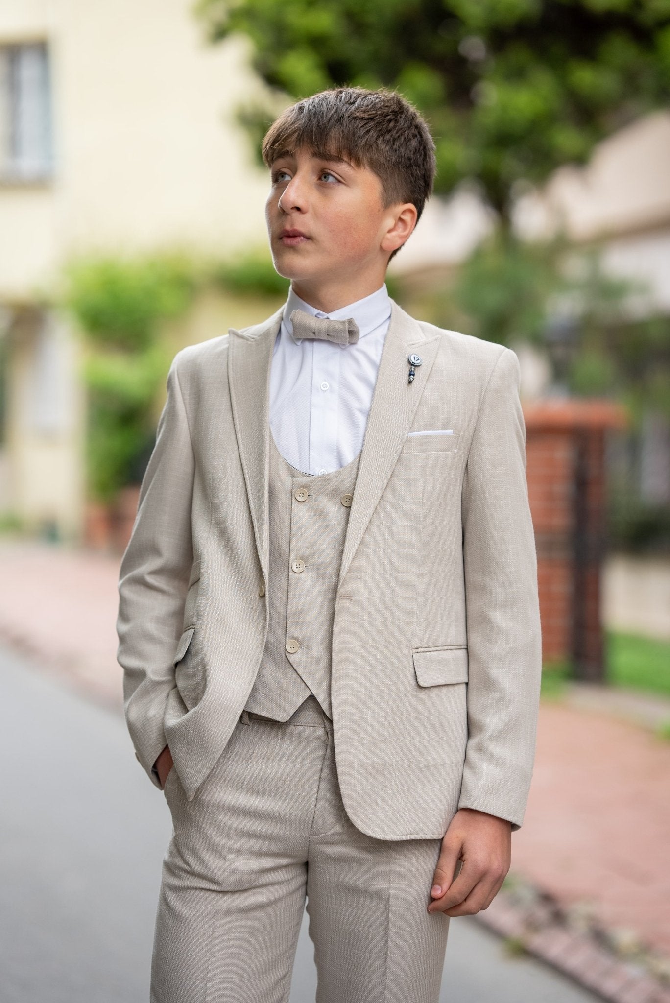Father and his two sons walking down a street in matching beige tuxedos with elegant bow ties, exuding confidence and style during a formal occasion.