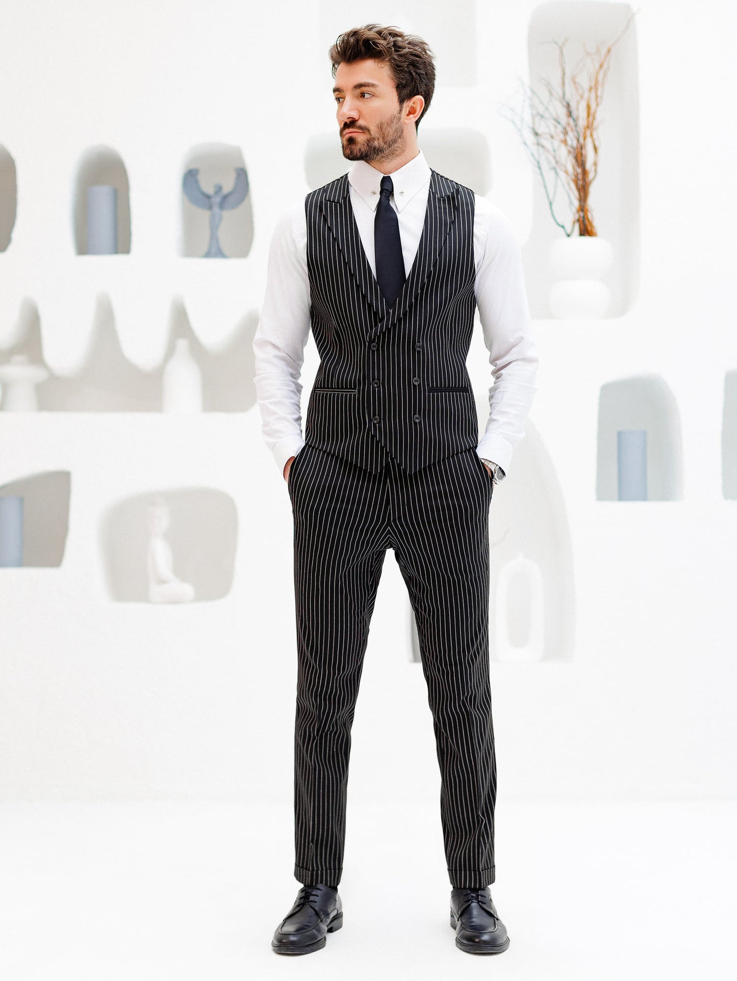 Men’s black pinstripe double-breasted vest with matching slim-fit trousers, styled with a white shirt and black tie for a modern formal look.