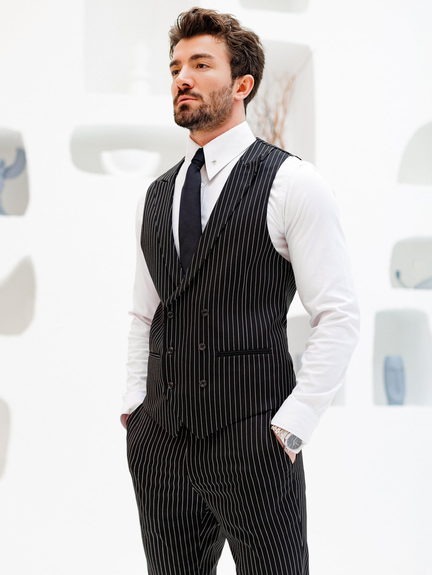 Men’s black pinstripe double-breasted vest with matching slim-fit trousers, styled with a white shirt and black tie for a modern formal look.