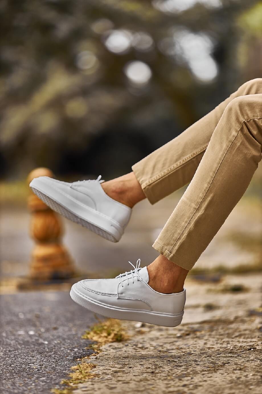 White leather lace-up casual derby shoes worn with beige chinos, photographed outdoors on a city street.