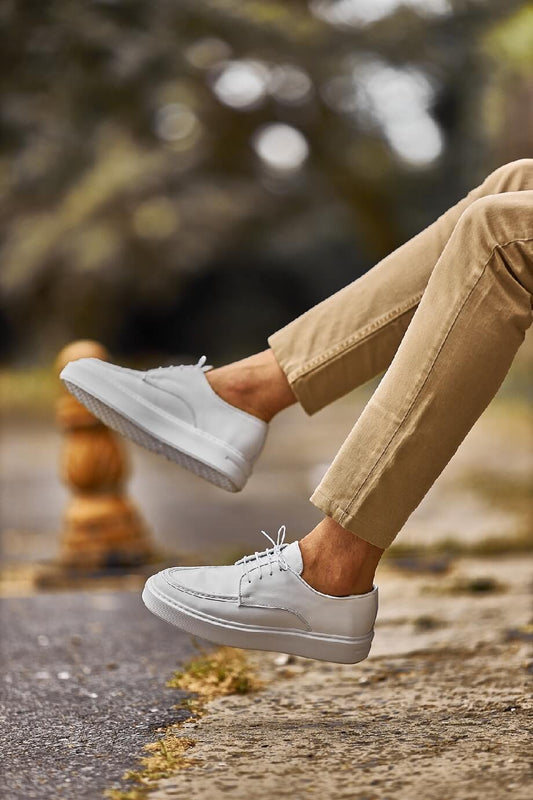White leather lace-up casual derby shoes worn with beige chinos, photographed outdoors on a city street.